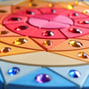 Grimm’s Sparkling Mandala Sun Creative Puzzle pieces are arranged in a circular mandala pattern, featuring inlaid colorful acrylic gemstones to support fine motor skills.