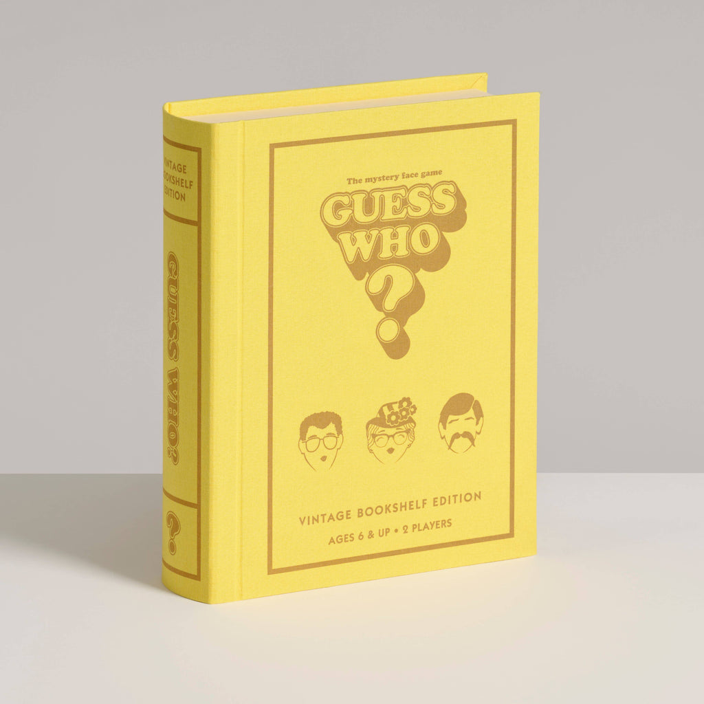 A yellow, book-shaped box labeled "Board Game: Guess Who? Vintage Bookshelf Edition" displays three face illustrations and stands upright on a white surface, styled to resemble a classic book.