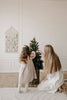 A young girl and a woman with long hair decorate a small Christmas tree in a cozy, minimalist room, placing Sabo Concept Christmas Ornaments amid the white walls and wooden floors.