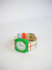 The Mini Kyomo Watch x Taxi Brousse - Color Notebook is a vintage style kids watch with a green plastic case and a cream fabric strap featuring red, blue, and green stripes, shown on a white background.