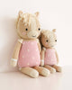 Two Cuddle + Kind Sophia the Pony dolls, hand knit in Peru from fair trade materials, feature beige bodies with pink flowered outfits and manes. The ponies, one large and one small, sit side by side against a white background.
