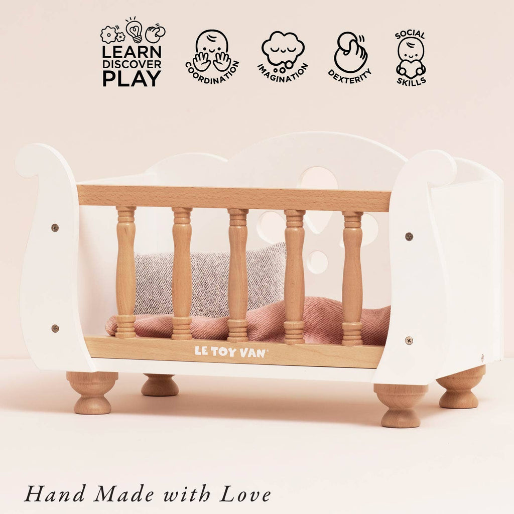 A Wooden Dolls Cot made of white wood with natural spindles, featuring a soft pink bedding set, displayed with five developmental skill icons above and the text “Hand Made with Love” below.