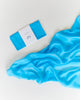 Sarah's Silks Solid Color Playsilk in Turquoise, made of pure silk, is presented folded in white packaging and alongside a matching draped cloth—ideal for open-ended play—displayed on a white surface.