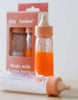 A pair of baby bottles, with one containing orange liquid and the other clear, are positioned in front of a pink package labeled "Bottled milk and juice set - Tiny Harlow." These bottles are ideal for enhancing doll feeding experiences. The softly blurred background accentuates the beauty of both the bottles and their packaging.