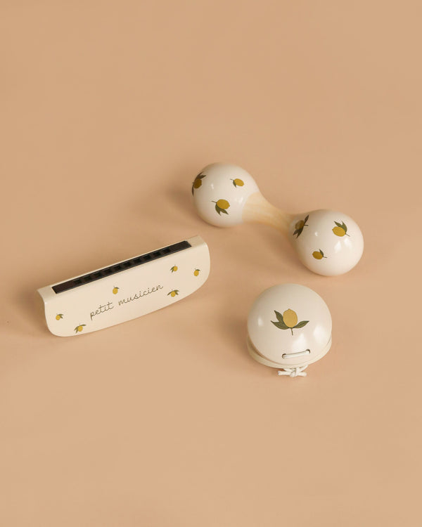 The Konges Sloejd Petit Music Set - Glossy Lemon, featuring three small cream-colored wooden instruments with yellow lemon patterns—a harmonica, kids’ maracas, and a jingle bell—rests on a light beige background.
