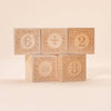 Five Uncle Goose Number Alphablank Blocks, each with a carved design, display the equation 6 ÷ 2 = 3. The educational toys are stacked in two rows against a neutral background.