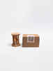 The Sabo Concept Rolling Rattle - Lagoon, a small wooden baby toy with vertical bars and colored balls inside, stands beside a plain brown box labeled with blue and orange dots, both set against a white background.