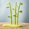 The Bumbu Handmade Wooden Red Panda Family with Bamboo Set features three stylized green bamboo stalks with leaves on a matching base—an ideal Montessori learning toy accent displayed on a wooden surface against a light blue background.