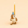 The Barn Owl Cake Topper – Final Sale is a handcrafted collectible ceramic owl figurine featuring a blue and white striped party hat and carrying a lit yellow candle on its back, displayed against a plain beige background.