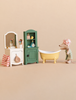 A Maileg Bathtub Set featuring a mouse in a shower cap standing next to a miniature yellow claw-foot bathtub, a green cabinet with a toothbrush set, and a white vanity with a mirror.