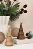 Two minimalist Spring Copenhagen The Christmas Tree, Oak ornaments with gold stars on top, one in light wood and one in dark wood, displayed on a table alongside holiday decorations.