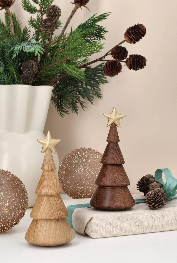 Two minimalist Spring Copenhagen The Christmas Tree, Thermo Beech ornaments, one light and one dark, each topped with a small gold-colored star.