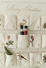 Wooden Soldiers advent calendar with embroidered pockets numbered 1 to 14, showcasing holiday motifs such as a reindeer, pinecone, and festive plants. Two wooden soldier figurines are tucked into pocket number 8.