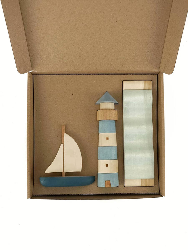 The Sabo Concept Sea Adventure Set features a sailboat, lighthouse toy, and striped block in blue, white, and natural wood tones, all neatly arranged in a brown open cardboard box.