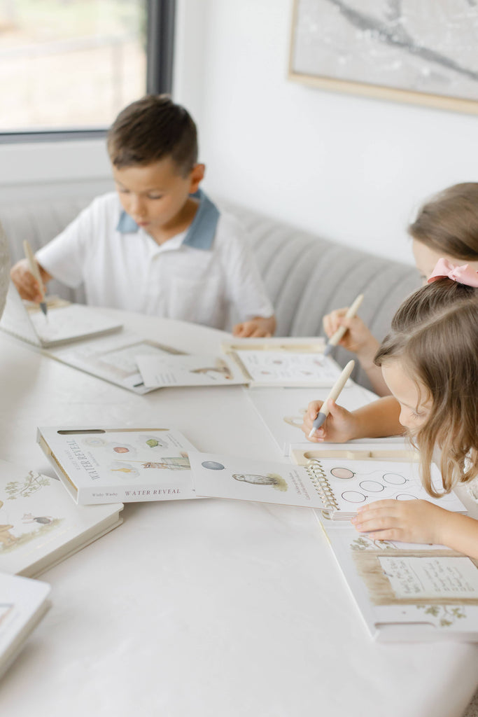 Two children sit at a table using Winnie-the-Pooh: Pooh’s Birthday Surprise (Water Reveal) books with specialized pens for a no-mess activity.