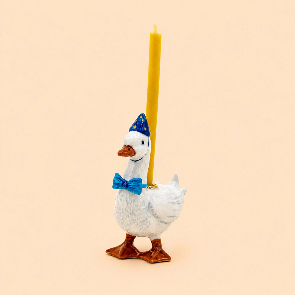 Introducing the Blue Goose Cake Topper - Final Sale: this charming porcelain decoration features a ceramic goose wearing a blue party hat and bow tie, carrying a yellow candle on its back, all set against a plain light beige background—a delightful handcrafted birthday keepsake and collectible.