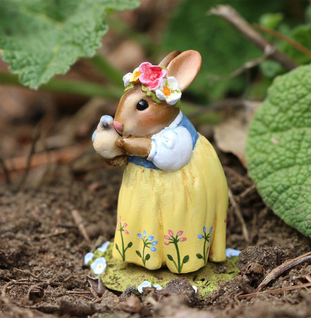 The Wee Forest Folk Tiny Collectible - Bluebird of Happiness (Not a Toy) features a hand-sculpted miniature rabbit in a yellow flower dress and crown, standing on soil with green leaves while holding a tiny bird.