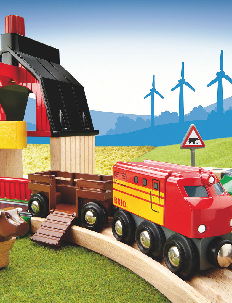 The BRIO World Train Set Farm Railway Set features a red and yellow "BRIO" engine, animal figures, tracks, a barn, wind turbines, and green and yellow play mats for imaginative farm-themed play.