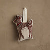 The Coral & Tusk Rudolph Ornament is a small, soft reindeer shaped like a fawn with a red collar and white spots, hanging by a cream loop against a textured beige wall.