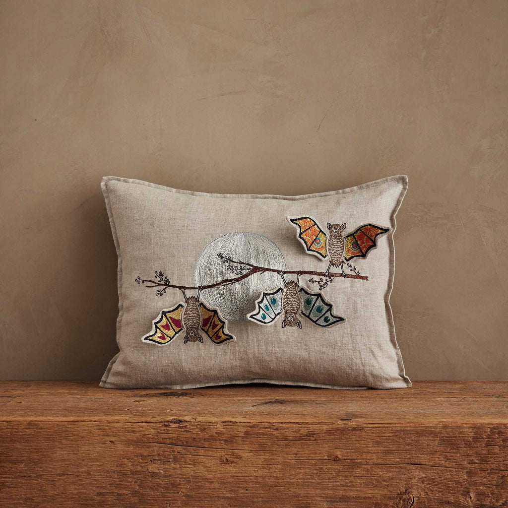 The Coral & Tusk Bat Branch Pillow, a rectangular beige cushion featuring embroidered baby bats hanging from a branch beneath a full moon, is perfect for Halloween décor on rustic surfaces. Ships in one week.