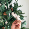 A hand holds a Finger Puppet: Shark in front of a green Christmas tree with pinecones, inviting imaginative underwater play amid festive holiday decor.