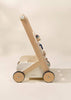 The Wooden Activity Walker features four black wheels, a handlebar, and attached sensory toys for engaging play, set against a soft beige background.