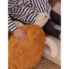 A child in a black and white striped dress sits on a mat, gently resting a hand on the Senger Naturwelt Cuddly Animal - Turtle, which is made with soft organic cotton and filled with a grain pillow.