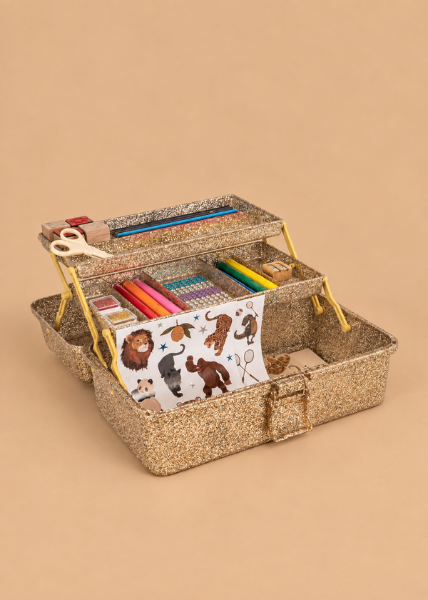 The Konges Sloejd Creative Art Caddy - Tiger, an open glittery gold toolbox filled with kids’ art supplies—colored markers, crayons, scissors, a ruler, glue, and a sheet of animal stickers—invites imaginative play on a beige background.