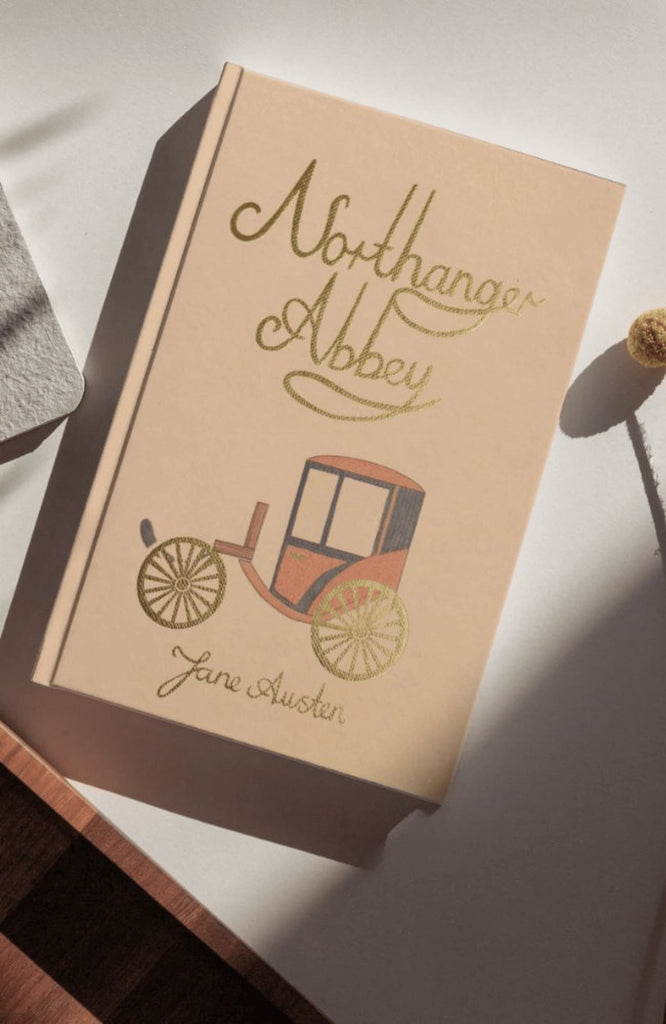 A beige "Northanger Abbey | Collector's Edition | Hardcover" with a vintage carriage illustration rests on a sunlit white surface.