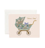 The Floral Pram Card features a vintage baby carriage adorned with vibrant flowers and a purple bow, gold foil "Welcome, Baby!" text, a blank interior for your message, and comes with a soft white envelope.