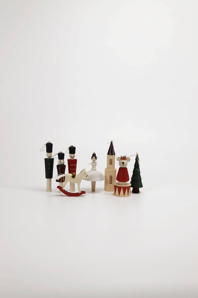 A set of Sabo Concept Christmas Ornaments, featuring hand-painted wooden pieces like a nutcracker set, ballerina, rocking horse, church, fir tree, and crown bear, arranged on a white surface with a minimalist background.