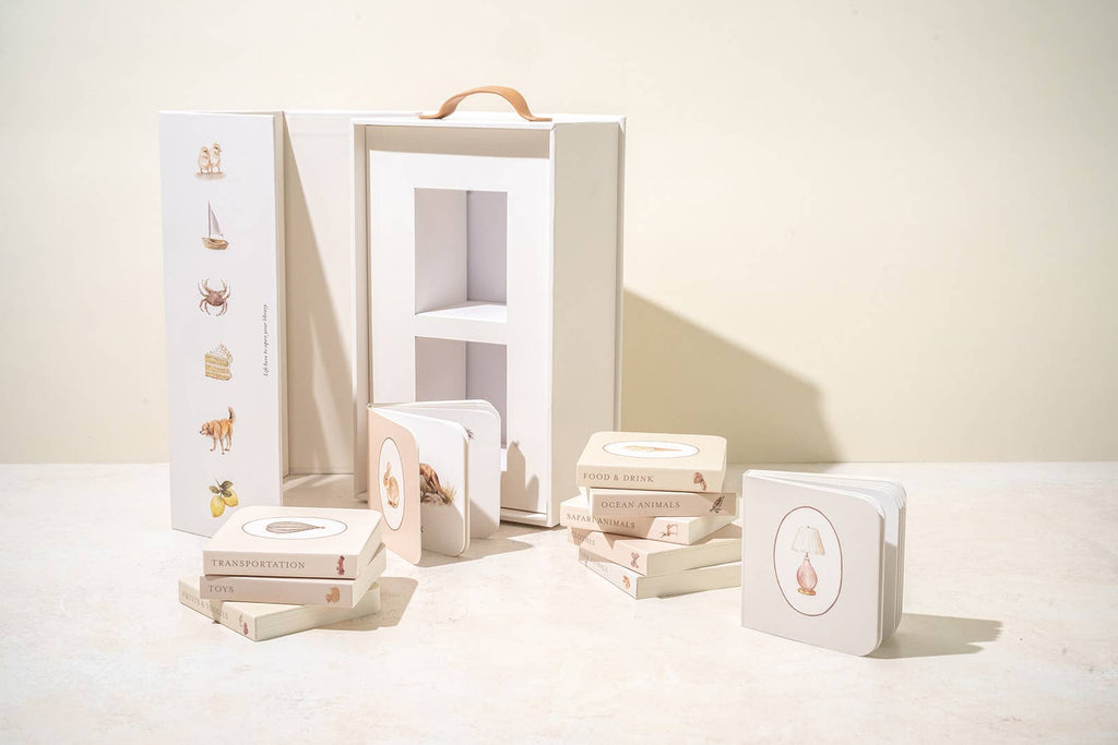 The Newborn Gift Set features small pastel board books with simple animal and object illustrations beside an open white carrying case, paired with a soft Maileg Plush Sleeping Bunny for extra charm.
