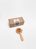 A brown cardboard box with a white label sits next to the Sabo Concept Lion Rattle - Natural, a baby toy crafted from natural materials, displayed on a white background.