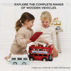 Two young children play with wooden vehicles, like a red London bus, a vintage campervan, and the Wooden Ice Cream Van (ships in one week), beneath text: "Explore the complete range of wooden vehicles.
