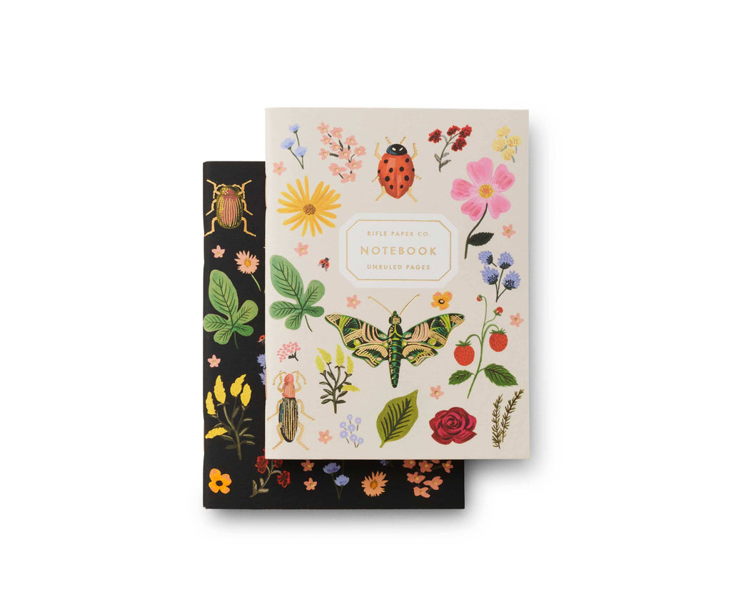 The Pair of 2 Curio Pocket Notebooks includes one cream and one black notebook, each featuring colorful illustrations of flowers, leaves, insects, and butterflies. Cream notebook label: "Rifle Paper Co. Notebook Unruled Pages." Size: 4.3 x 5.5 x 0.4 in.