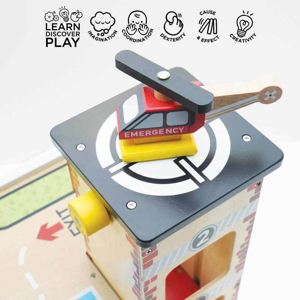 A wooden toy emergency helicopter rests on the Fire & Rescue Garage playset’s helipad. Above are icons that read: "LEARN DISCOVER PLAY," "IMAGINATION," "COORDINATION," "DEXTERITY," "CAUSE & EFFECT," and "CREATIVITY.