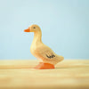 The Bumbu Handmade Wooden Domestic Duck features a small, handcrafted design with an orange beak and feet, black detailing on the eyes and wing, standing on a light wooden surface against a pale blue background.