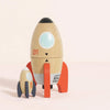 The Magnetic Space Rocket Duo features two wooden rockets, one with red fins and a window and the other with dark fins. Both are decorated with playful details, perfect for inspiring creative play on any light-colored surface.