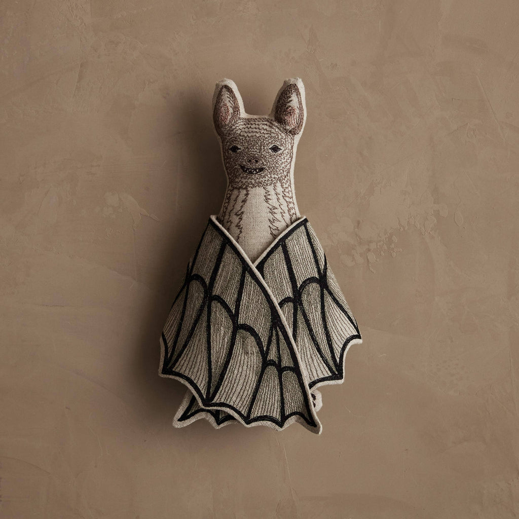 The Coral & Tusk Bat Surprise Doll is a soft plush bat with a stitched face and black-edged fabric wings, ideal as a cute decor piece or Halloween decoration. Ships in one week; shown on a textured beige background.