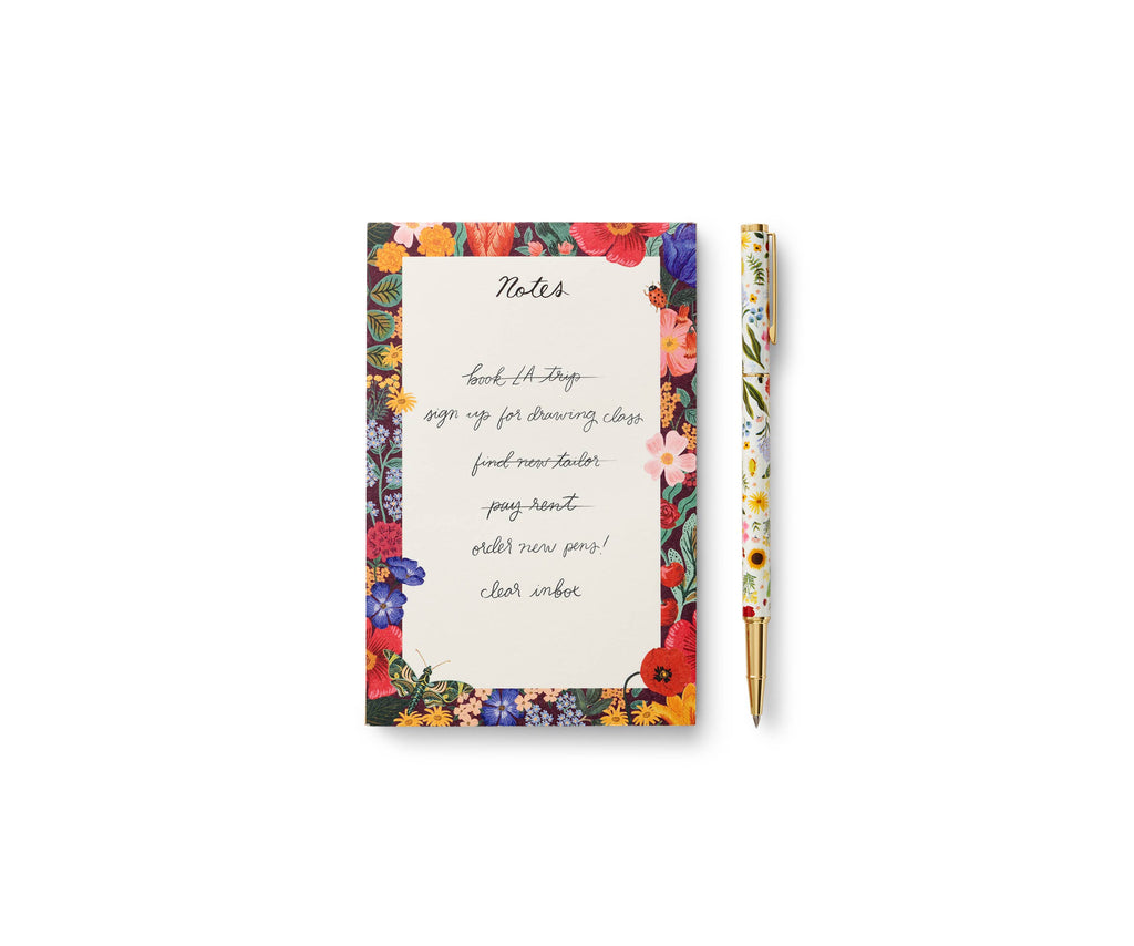 A floral notepad with handwritten notes sits next to a Curio Pen on a white background. The to-do list is written in cursive using the smooth, refillable black ink of the Curio Pen.