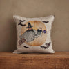 The Coral & Tusk Supermoon Spell Pillow features a witch and cat riding a broomstick before a large orange moon with bats, adding enchanting charm to your space against a plain brown background.