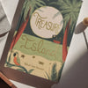 The "Treasure Island | Stevenson | Collector's Edition | Hardcover Book" rests on a white surface, featuring palm trees, a red ship, a parrot, a crab, and a golden sun on its tropical island-themed cover.