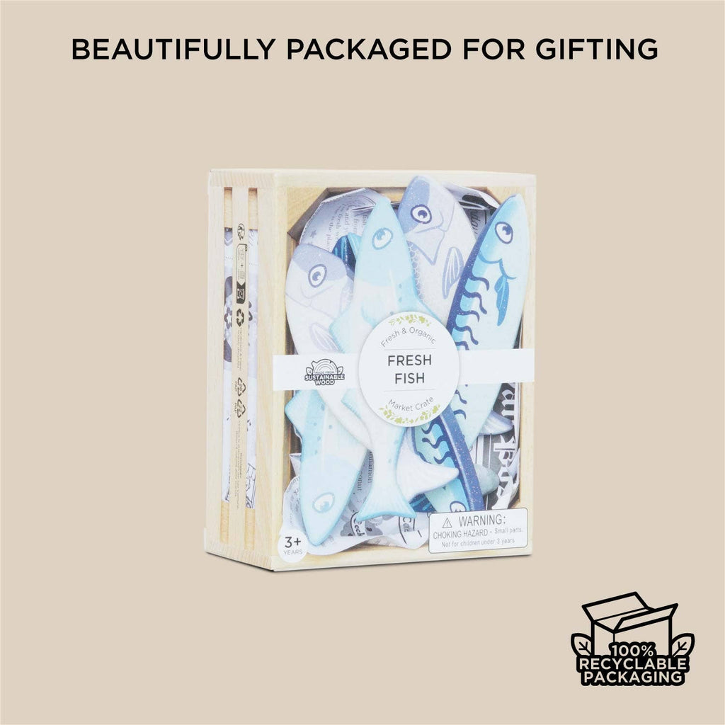 The Market Fish Wooden Play Market Crate, filled with toy fish and labeled "Fresh Fish," is displayed on a beige background with the text "Beautifully packaged for gifting" and a "100% recyclable packaging" icon in the corner.