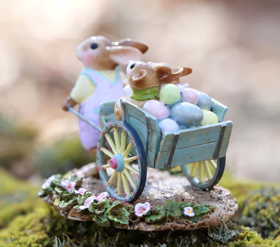 The Wee Forest Folk Tiny Collectible - Easter's on its Way (Not a Toy) features a hand-sculpted rabbit pushing a blue wheelbarrow with pastel eggs and a baby bunny on a mossy, flowered base—ideal for Wee Forest Folk fans.