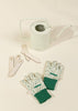 A Gardening Tools Playset, featuring a pale green watering can, floral garden gloves with green cuffs, and wooden plant markers, is arranged on a light beige surface.
