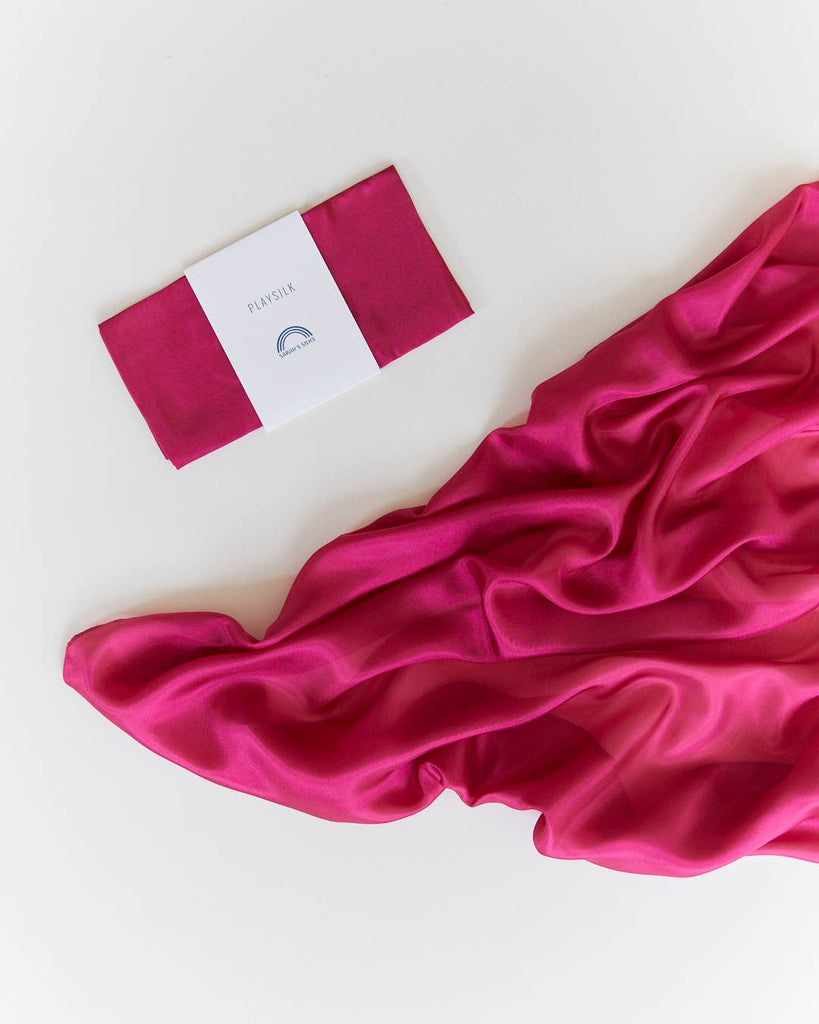 A folded Sarah's Silks Solid Color Playsilk in Red Violet with a white label sits beside a larger piece of matching sheer fabric on a white surface—perfect for open-ended play.