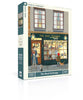 The Book Exchange - 1000 Piece Jigsaw Puzzle features an illustrated bookstore storefront with people and a dog—a charming bookshop puzzle and perfect gift for book lovers.