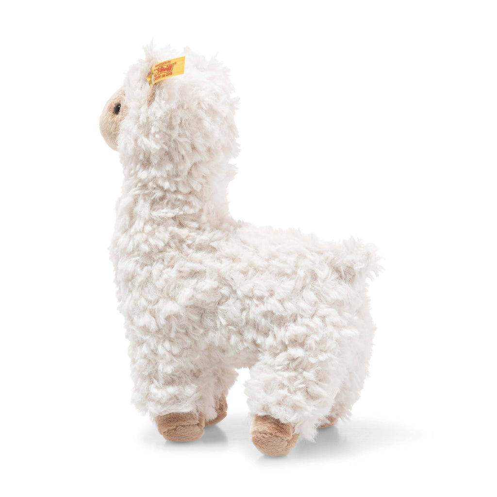 The Steiff Leandro Llama Plush Toy, 7 inches tall, stands on all fours with white, curly fur and beige face and feet. It features a signature yellow ear tag—perfect for fans of soft, cuddly companions.