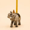 The Elephant Cake Topper - Final Sale (ships in one week) is a hand-painted ceramic figurine wearing a striped party hat with a yellow candle on its back, perfect as a whimsical collectible keepsake.