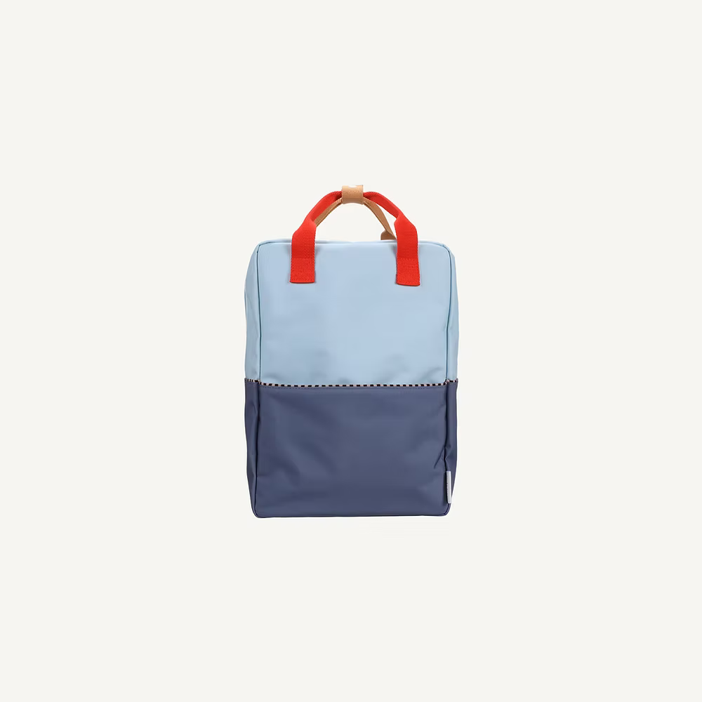 The Sticky Lemon Backpack Large | Color Blocking | Bissou Blue + Blue Whale is a rectangular kids backpack made from recycled PET bottles, with light blue and dark blue color blocks, red handles, and a tan loop, shown on a white background.